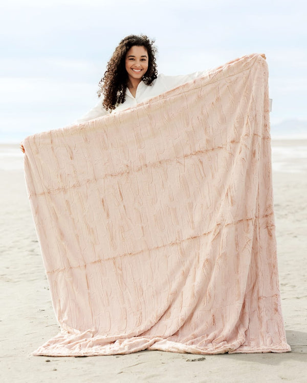 Woman showcasing a Sorbet Blush Pink Blanket at the beach, highlighting its soft, textured fabric and delicate hue.