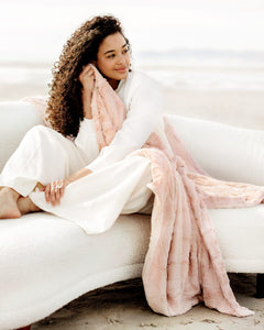Woman enjoying the Sorbet Blush Pink Blanket by the beach, showcasing its soft texture and gentle blush color.