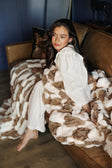 Cozy scene with a woman lounging on a sofa draped in a Hugs Check Milk Chocolate Blanket.