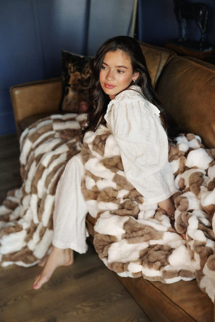 Cozy scene with a woman lounging on a sofa draped in a Hugs Check Milk Chocolate Blanket.