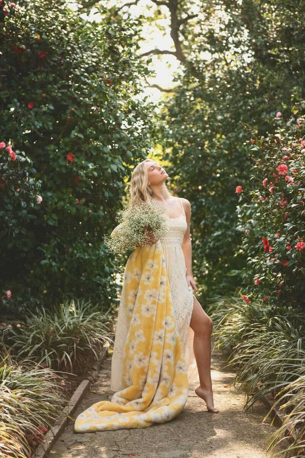 Lush Butter Yellow Floral Blanket draped over a woman in a garden surrounded by flowers.