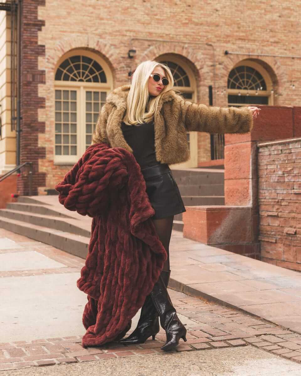 Person wearing a warm brown fur Hugs Rich Mahogany Blanket posing with a brick building in the background.