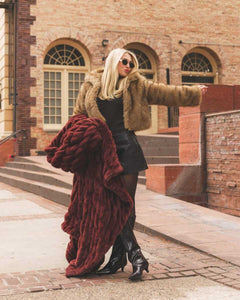 Person wearing a warm brown fur Hugs Rich Mahogany Blanket posing with a brick building in the background.
