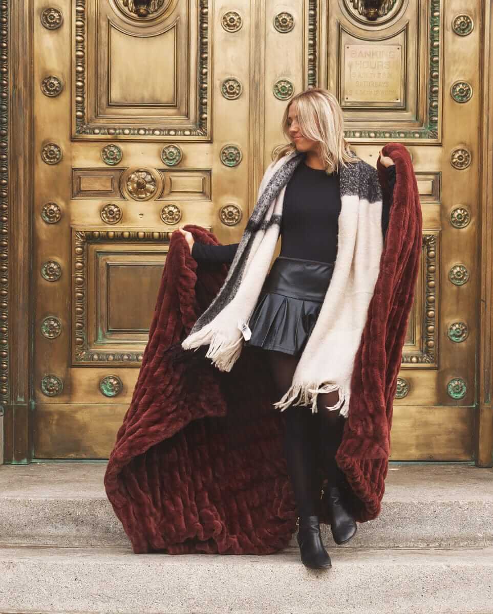 Woman holding a large warm brown Hugs Rich Mahogany fur blanket in front of an ornate gold door.