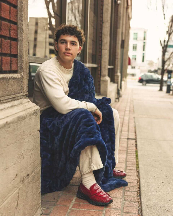 Young man sitting outdoors wrapped in Biggest Hugs Navy weighted blanket, showcasing comfort and style.
