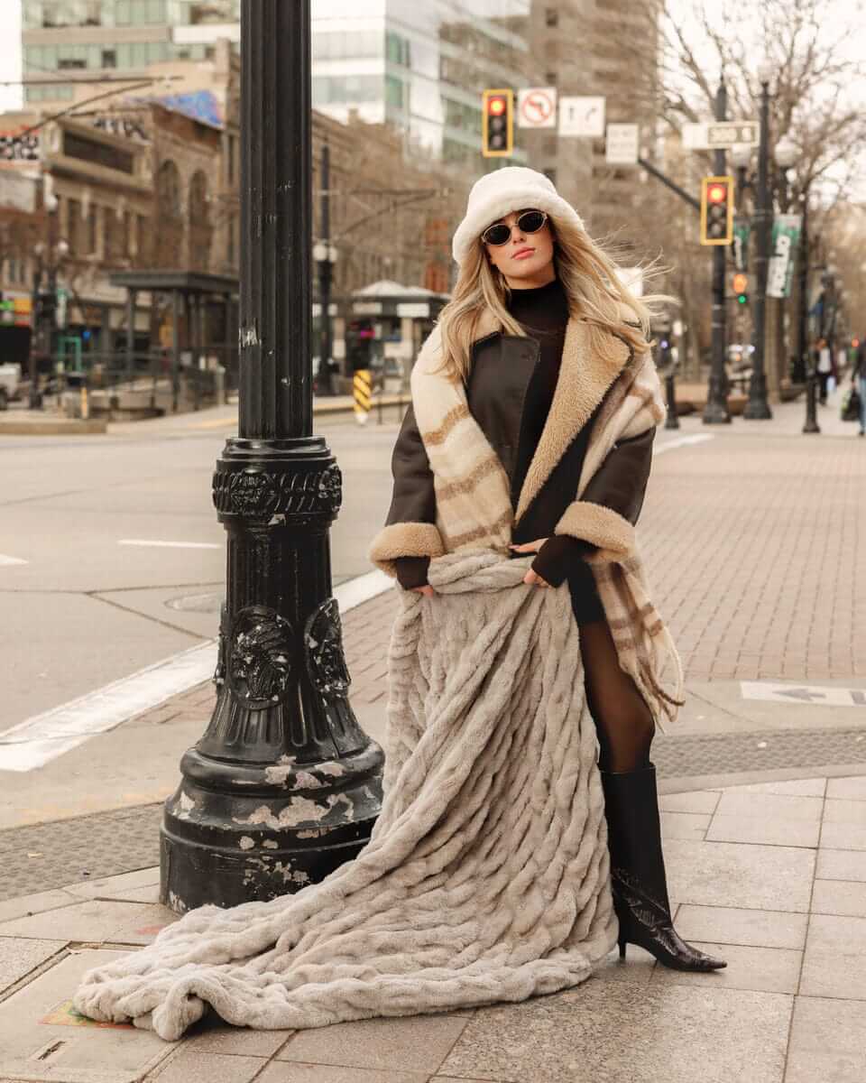 Woman in stylish coat showcasing the Biggest Hugs Tranquil Dove weighted Blanket in a city street.