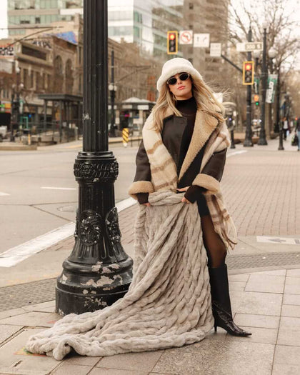 Woman in stylish coat showcasing the Biggest Hugs Tranquil Dove weighted Blanket in a city street.