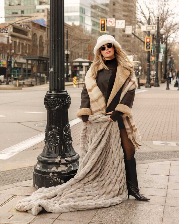 Woman in stylish coat showcasing the Biggest Hugs Tranquil Dove weighted Blanket in a city street.