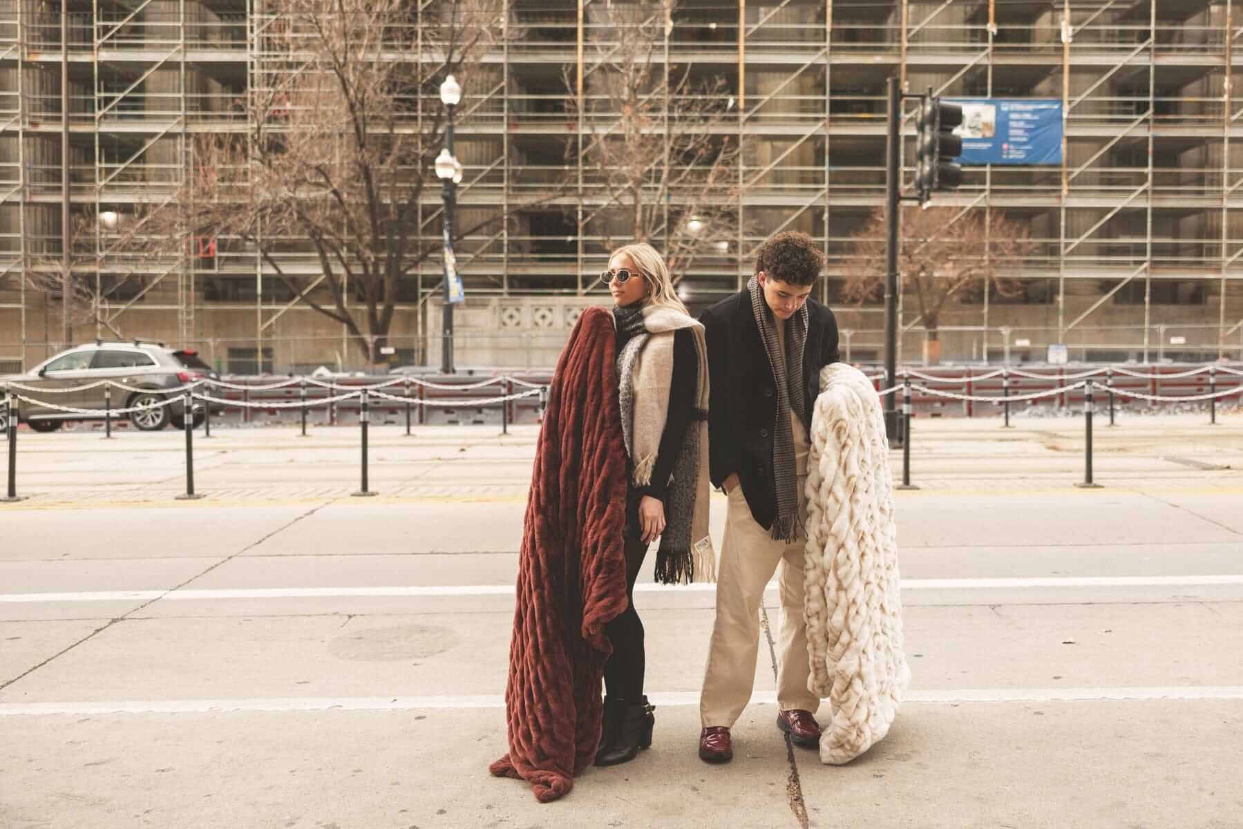 Two people standing on a city street with large warm brown and cream Hugs Minky Couture blankets.