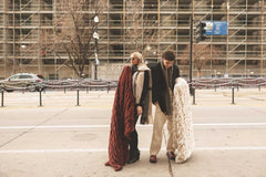 Two people standing on a city street with large warm brown and cream Hugs Minky Couture blankets.