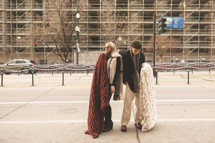 Two people standing on a city street with large warm brown and cream Hugs Minky Couture blankets.