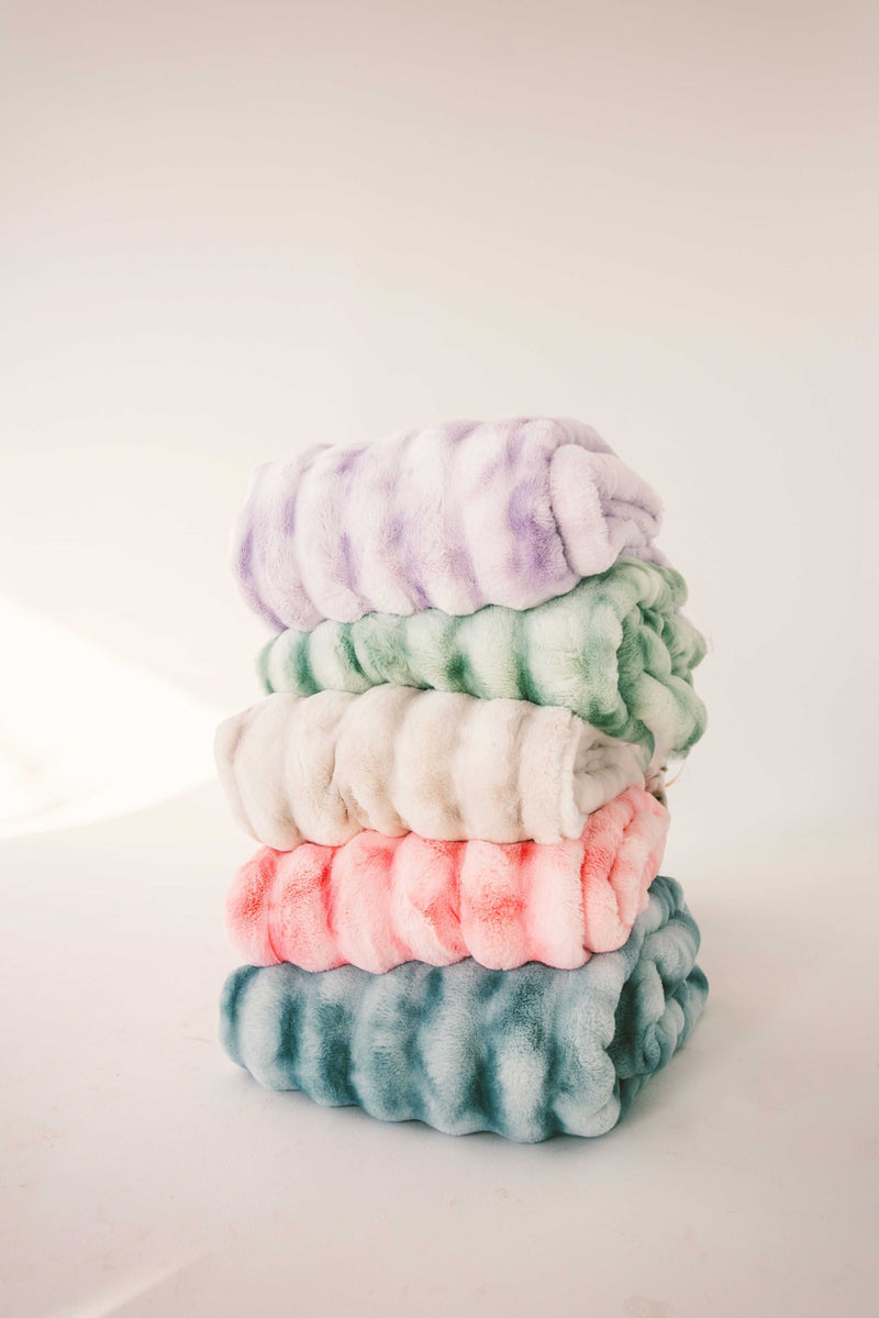 Stack of fluffy weighted blankets in pastel colors, including shades of pink, green, and lavender. Ideal for cozy moments.