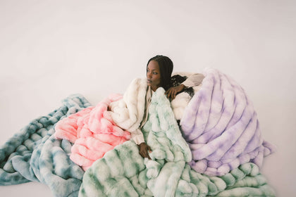 A woman surrounded by colorful plush blankets, showcasing vibrant shades of green, pink, and purple for optimal comfort.