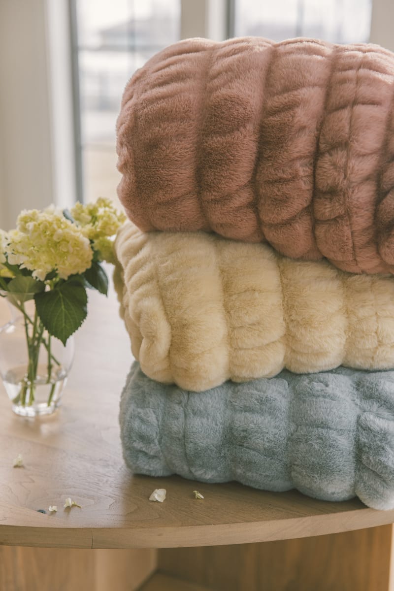 Stack of textured towels in pink, beige, and blue on a wooden surface with flowers in the background.