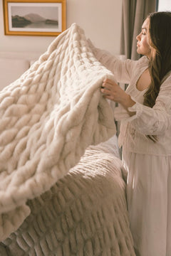 Woman holding a textured beige blanket in a bedroom setting.