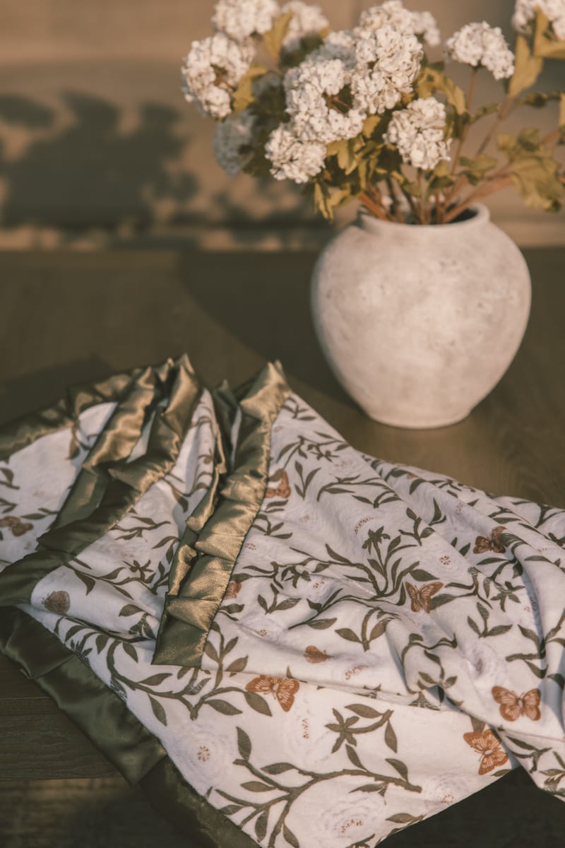 Vase with white flowers on a table with peony patterned blanket.