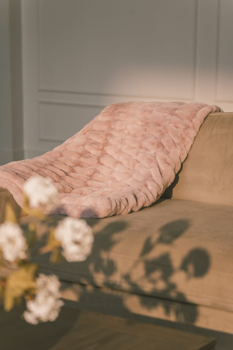 Pink textured blanket draped over a sofa with a neutral background.