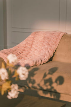 Pink textured blanket draped over a sofa with a neutral background.