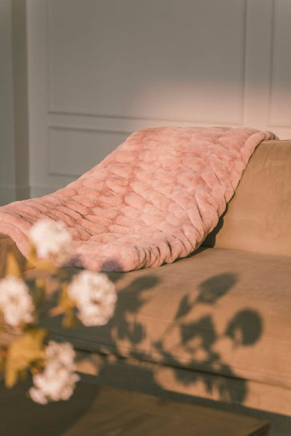 Pink textured blanket draped over a sofa with a neutral background.