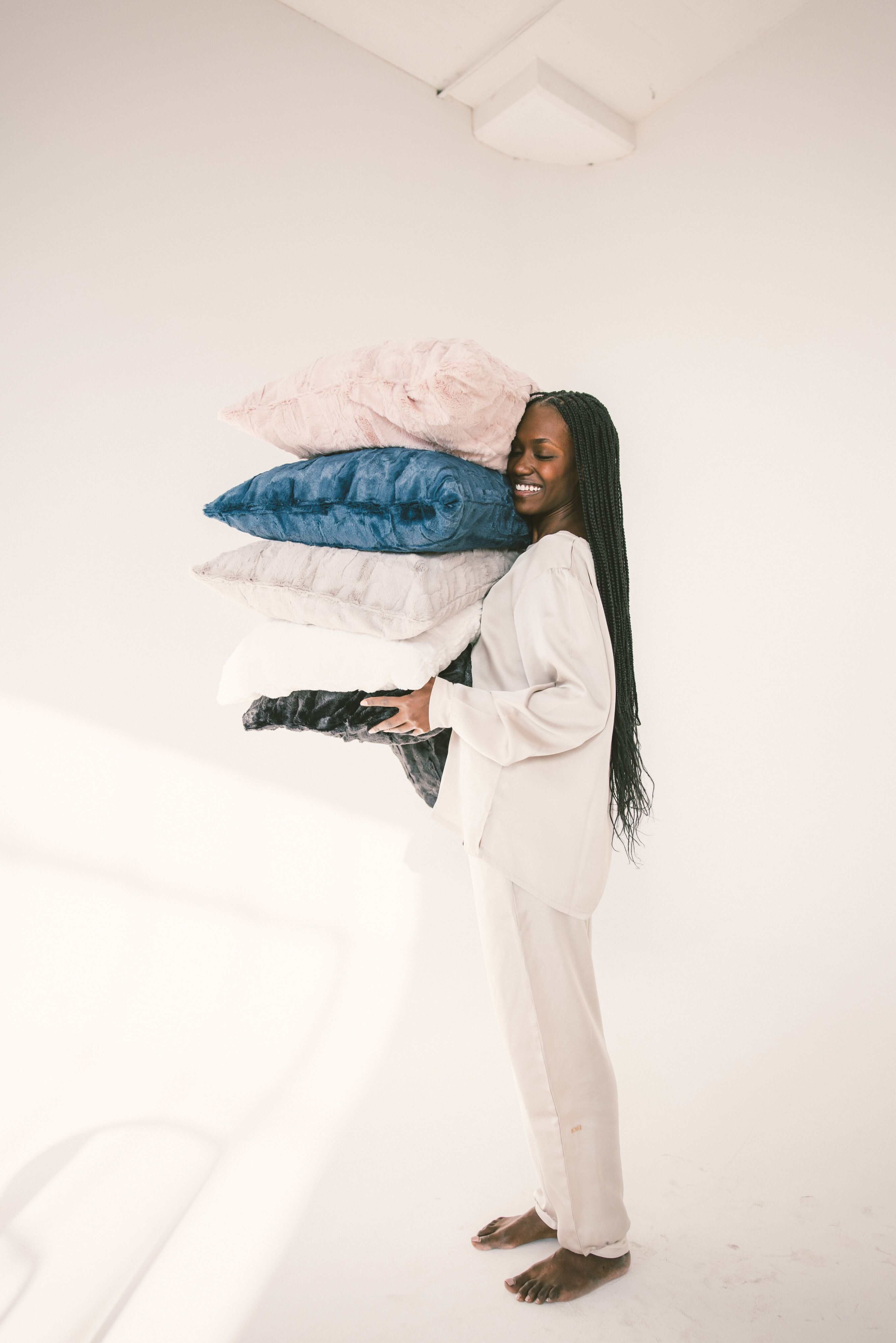 A smiling woman holding a stack of colorful Sorbet Pillowcases, showcasing luxurious bedding options.