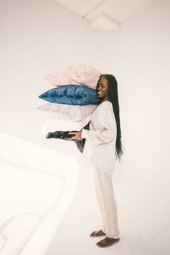A smiling woman holding a stack of colorful Sorbet Pillowcases, showcasing luxurious bedding options.