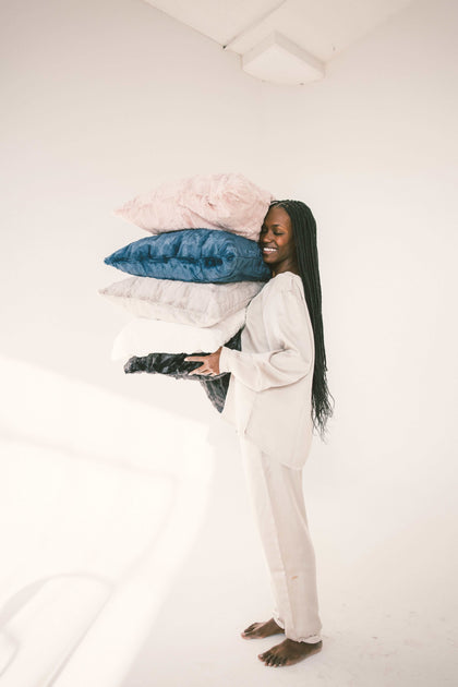 A smiling woman holding a stack of colorful Sorbet Pillowcases, showcasing luxurious bedding options.