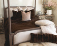 Decorative bedroom with a four-poster bed, brown and white bedding, and a nightstand with a lamp.
