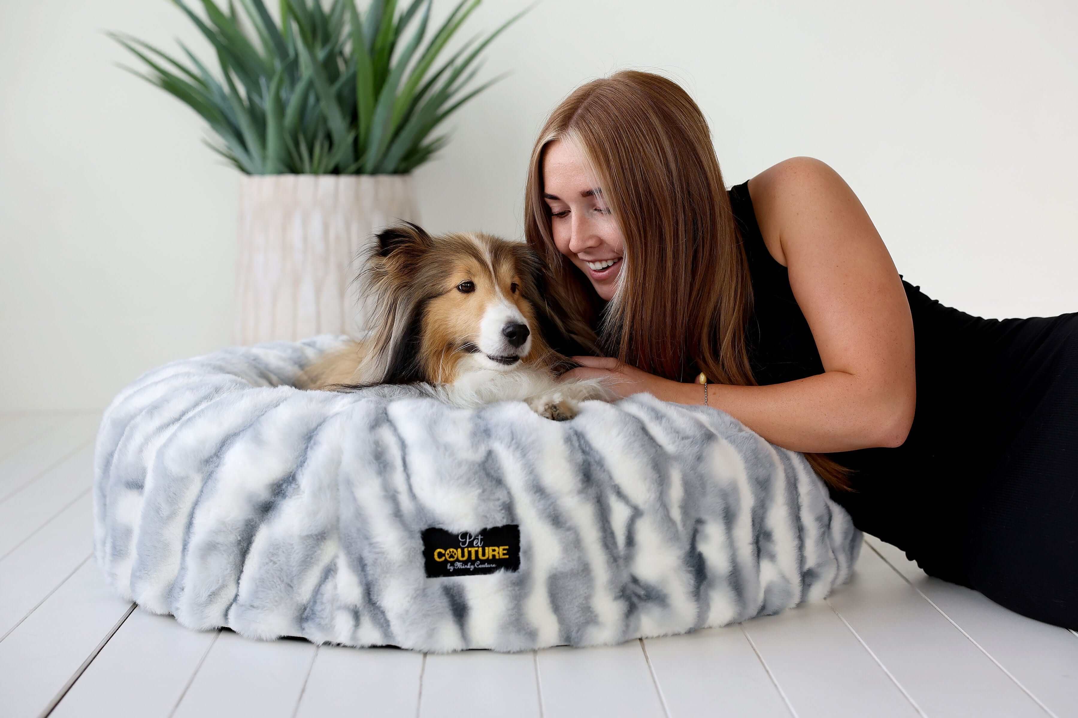 Minky Couture Cloudy Day Blue Pet Bed cover on a fluffy bed with a smiling woman and her pet dog.