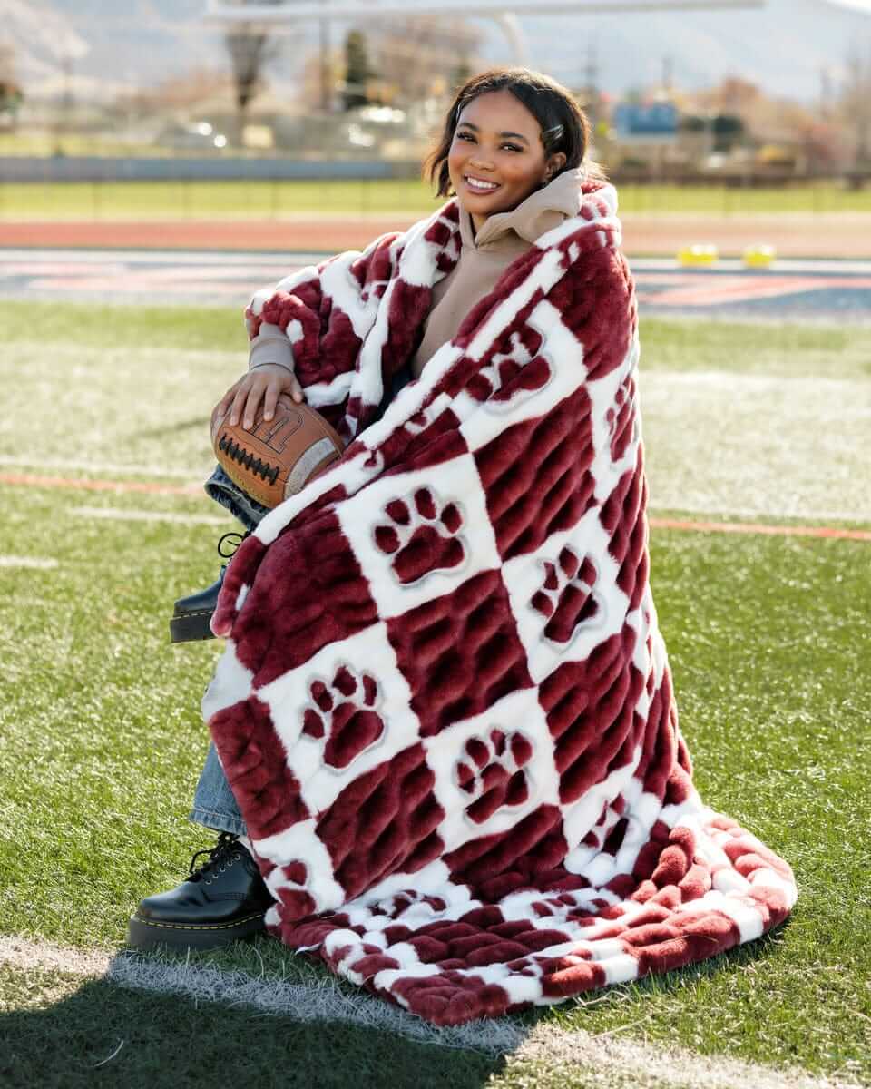 A person wrapped in a cozy Mississippi State Bulldogs Blanket featuring a maroon and white checkered pattern.