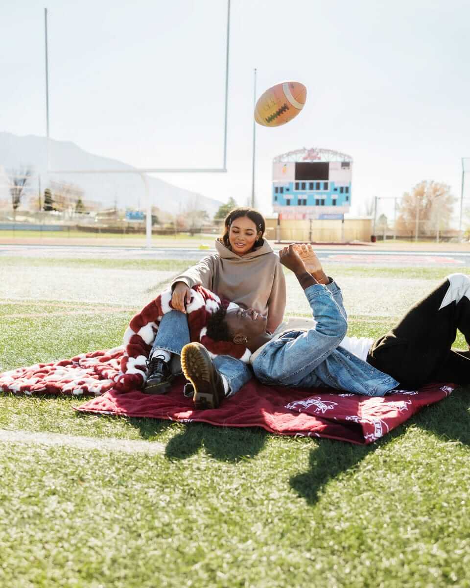 Two people enjoying the Mississippi State Bulldogs Hooded Stadium Blanket on a football field.