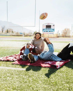 Two people enjoying the Mississippi State Bulldogs Hooded Stadium Blanket on a football field.