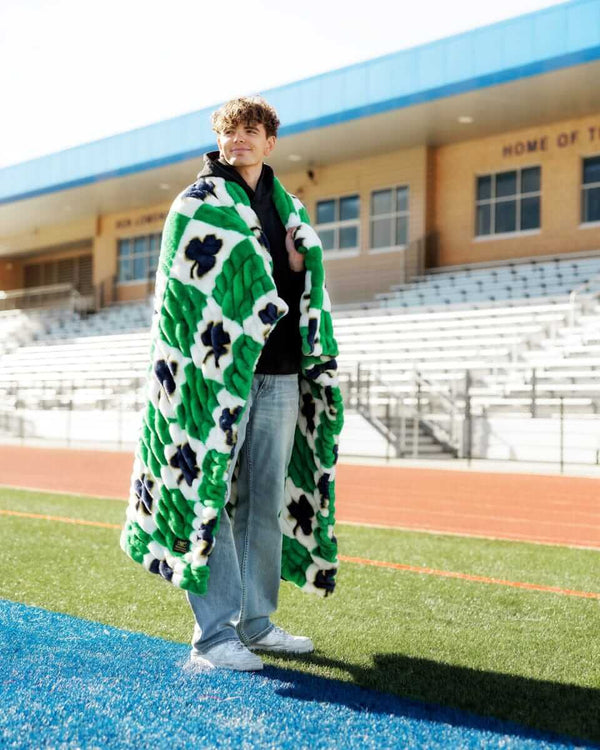Hugs Notre Dame Fighting Irish Blanket displayed by a person on a sports field, showcasing team pride and cozy style.