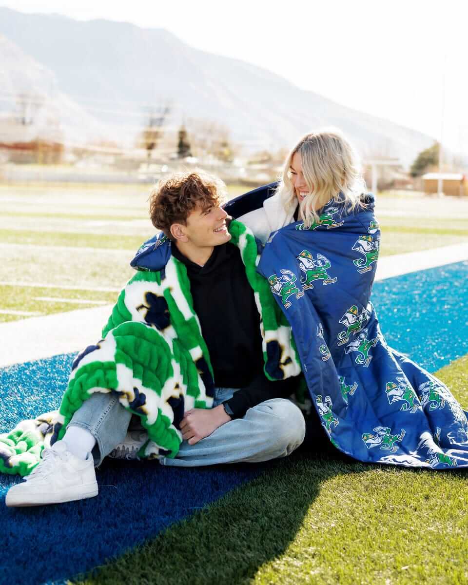 Notre Dame Fighting Irish Hooded Stadium Blanket used by a couple outdoors on a sunny day.