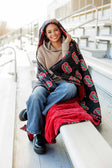 Person sitting on stadium bleachers wrapped in Stanford Cardinals Hooded Stadium Blanket.