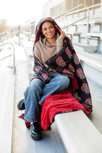 Person sitting on stadium bleachers wrapped in Stanford Cardinals Hooded Stadium Blanket.