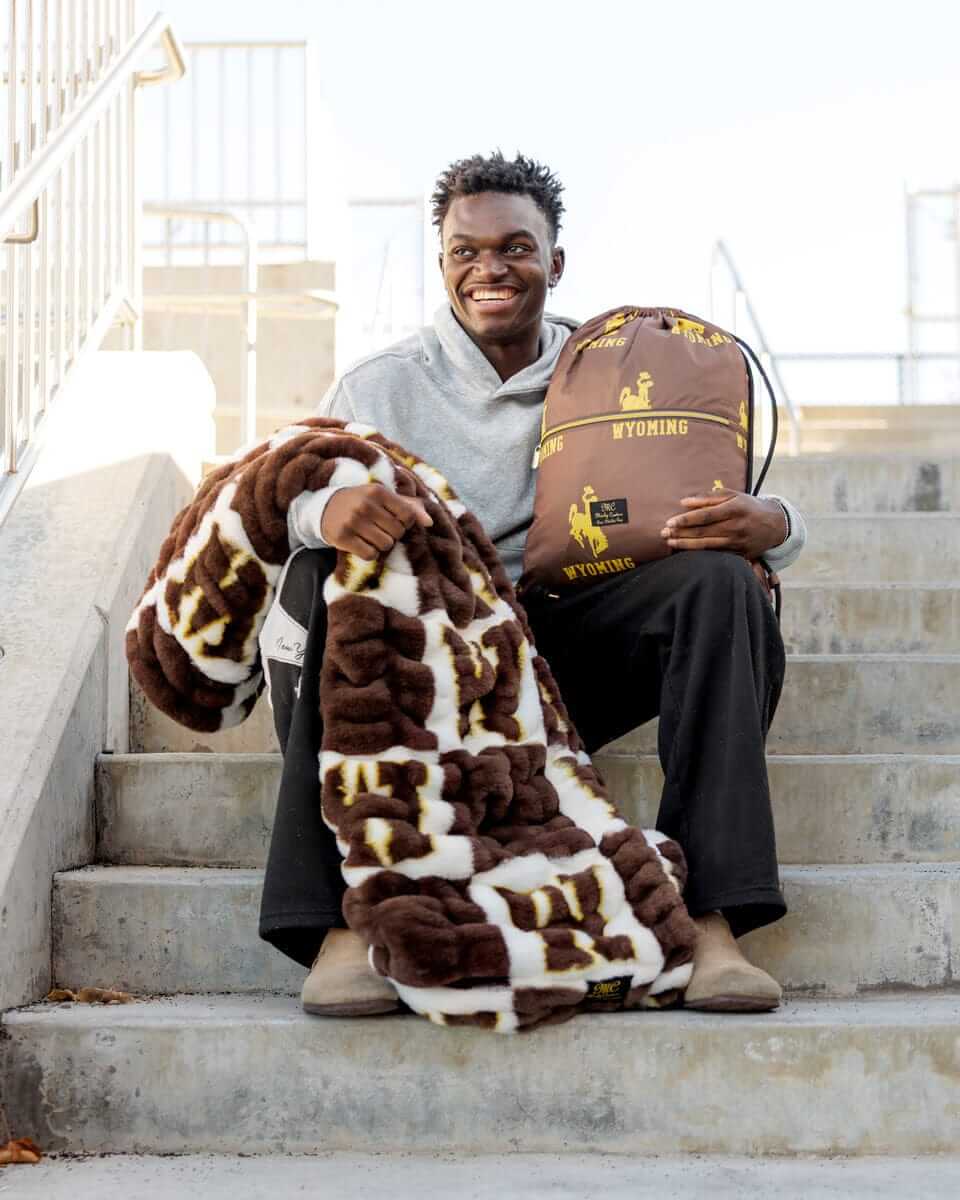 Wyoming Cowboys Hooded Stadium Blanket, shown on a person sitting on stairs, highlighting warmth and comfort.