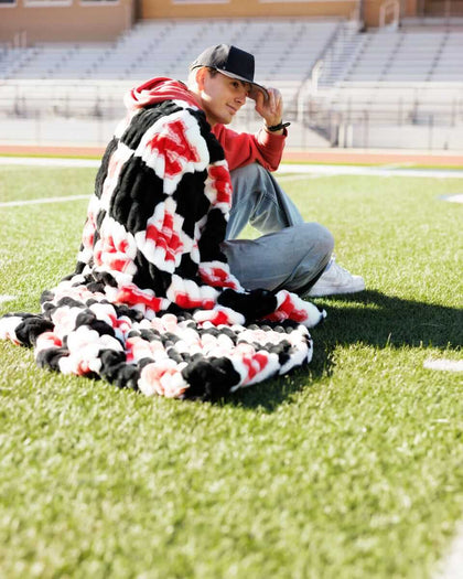 Nebraska Huskers Blanket draped over a person sitting on a football field, showcasing its bold black, white, and red design.