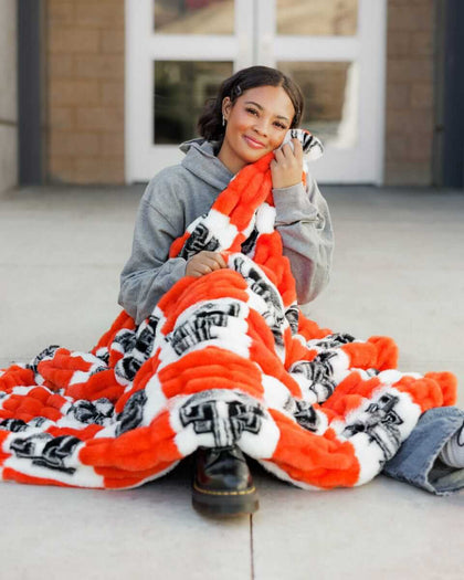 Hugs Texas Tech Raiders Blanket with a smiling woman wrapped in a cozy, patterned blanket.