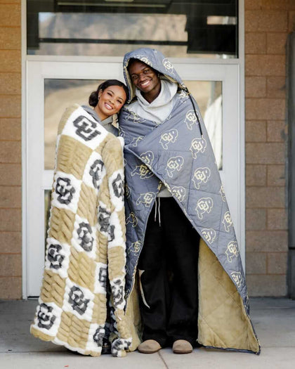 Two people wearing Colorado Buffaloes Hooded Stadium Blanket, showcasing warmth and team spirit.