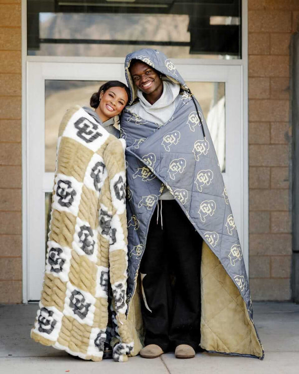 Two people wearing Colorado Buffaloes Hooded Stadium Blanket, showcasing warmth and team spirit.