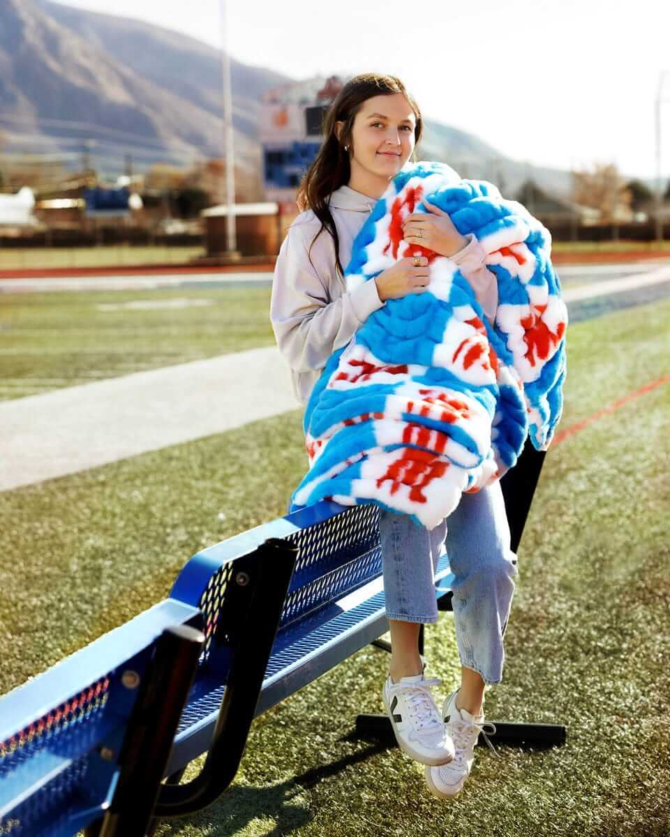A girl holding a Hugs Ole Miss Rebels Blanket featuring a blue and white checkered design with red accents.