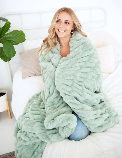 Woman wrapped in a cozy Hugs Mist Blanket in soothing sage green color, perfect for relaxation.