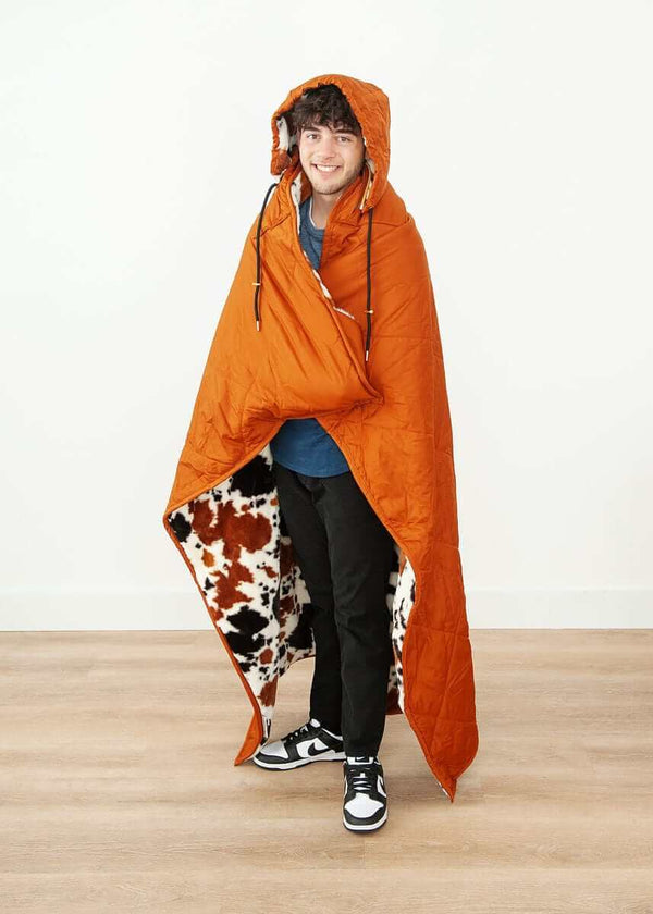Cozy man wearing the Everywhere Blanket Brown Cow with a plush cow print interior and hood.