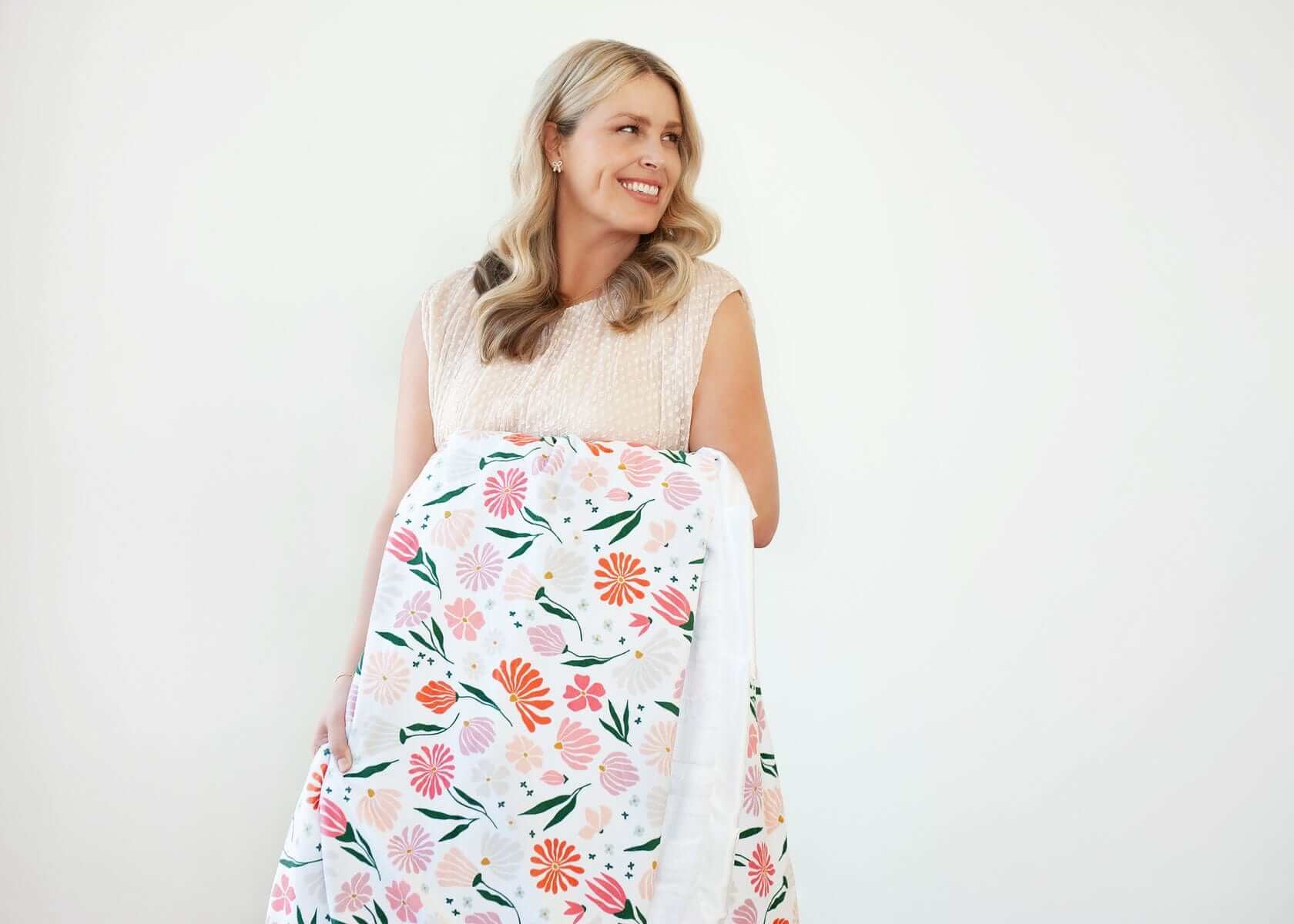 Woman smiling while holding the Baby Bloom Blanket with floral pattern, perfect for cozy moments.