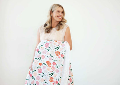 Woman smiling while holding the Baby Bloom Blanket with floral pattern, perfect for cozy moments.