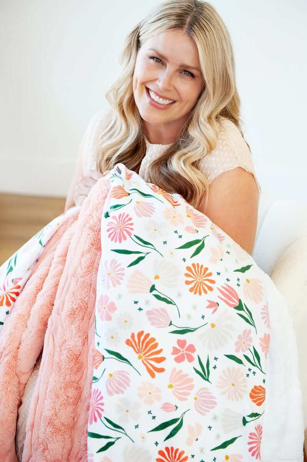 Woman smiling while holding the Baby Bloom Blanket featuring vibrant floral designs.