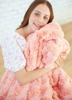 Woman cherishing the Ultra Sorbet Spring Blossom Blanket in a soft pink hue, showcasing its plush texture and cozy elegance.