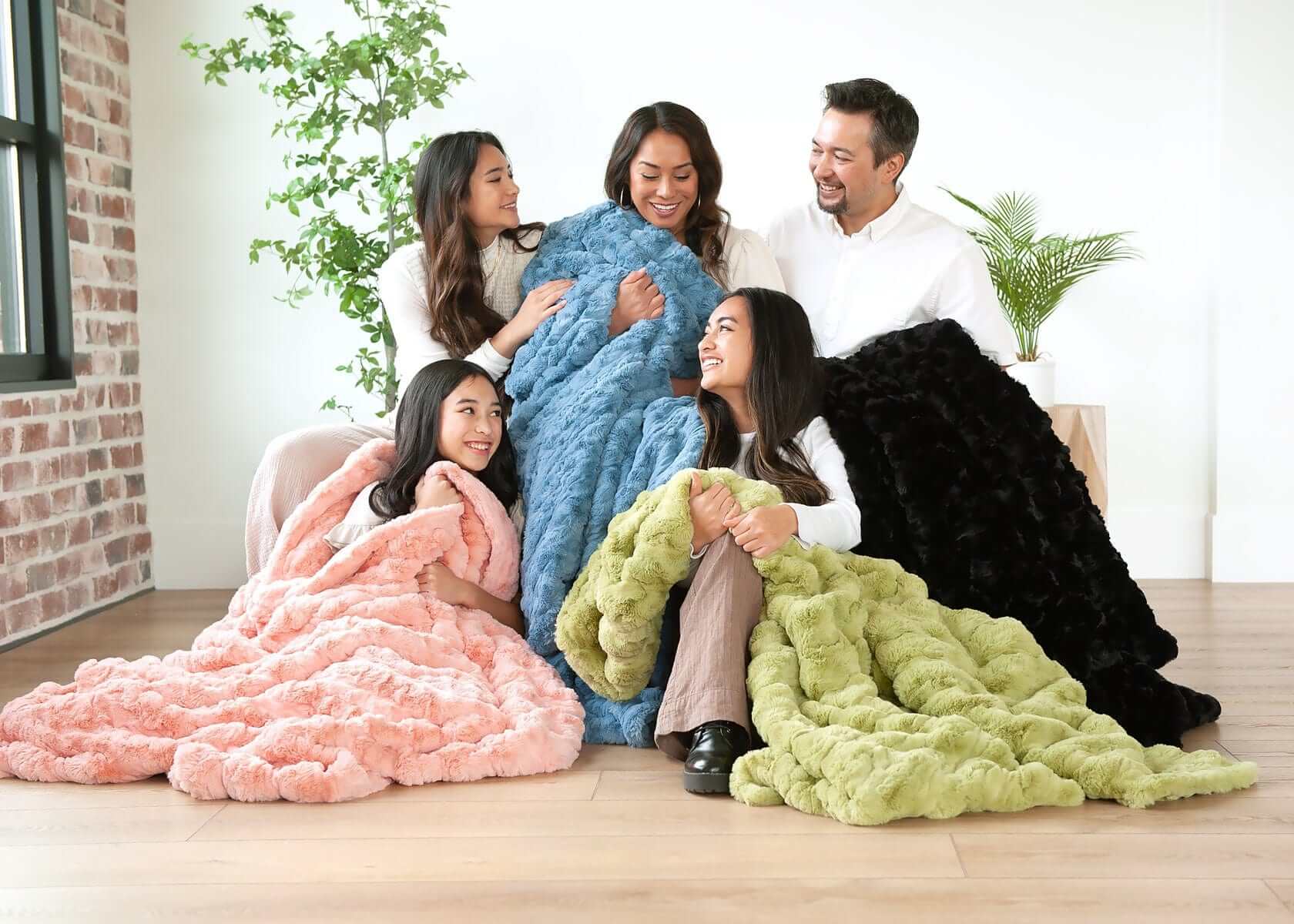Young family sitting together while wrapped up in four different colored blankets.
