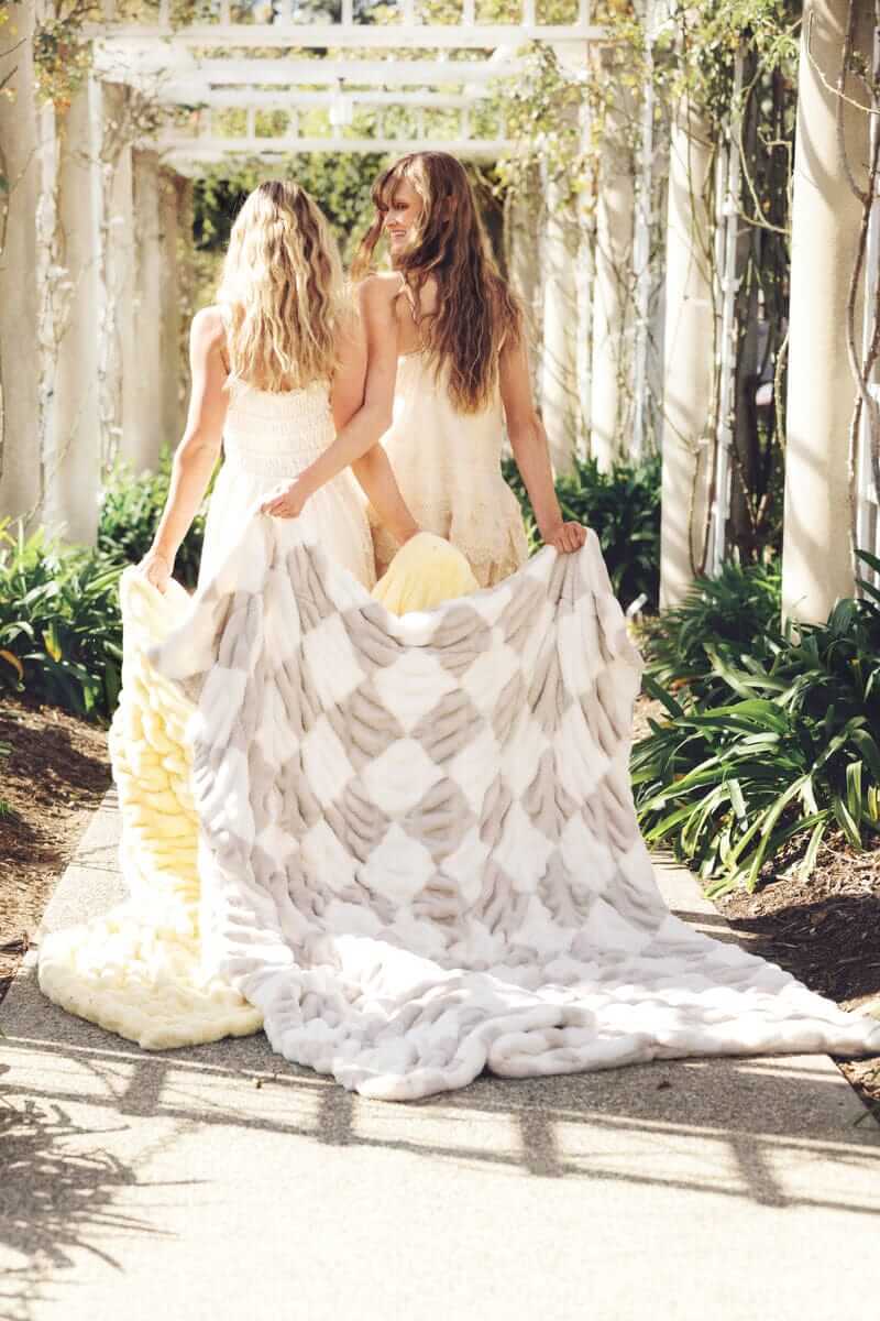 Two women holding the Minky Couture Hugs Diamond Ancient Scroll Blanket in a garden setting.
