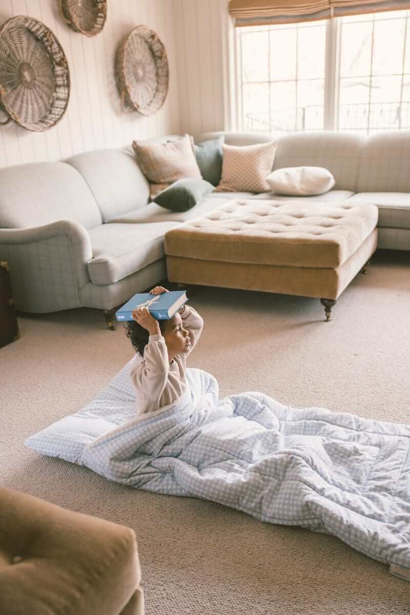 Child playing with a book on a Sleeping Bag Dusty Blue Gingham in a cozy living room setting.